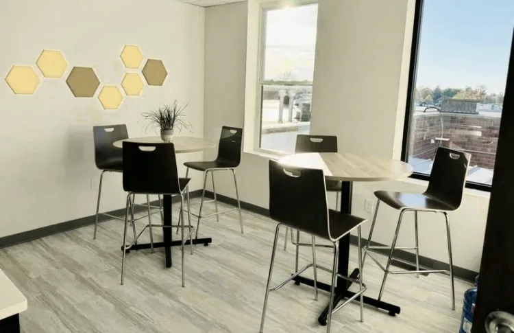 A bright common area with two high tables, stools, hexagon wall panels and large windows looking out over Hillsboro.