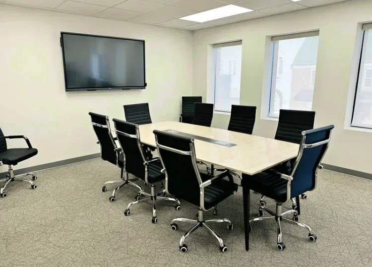 A meeting room at Changes Counseling with a long table, eight chairs, a wall-mounted screen and two windows.